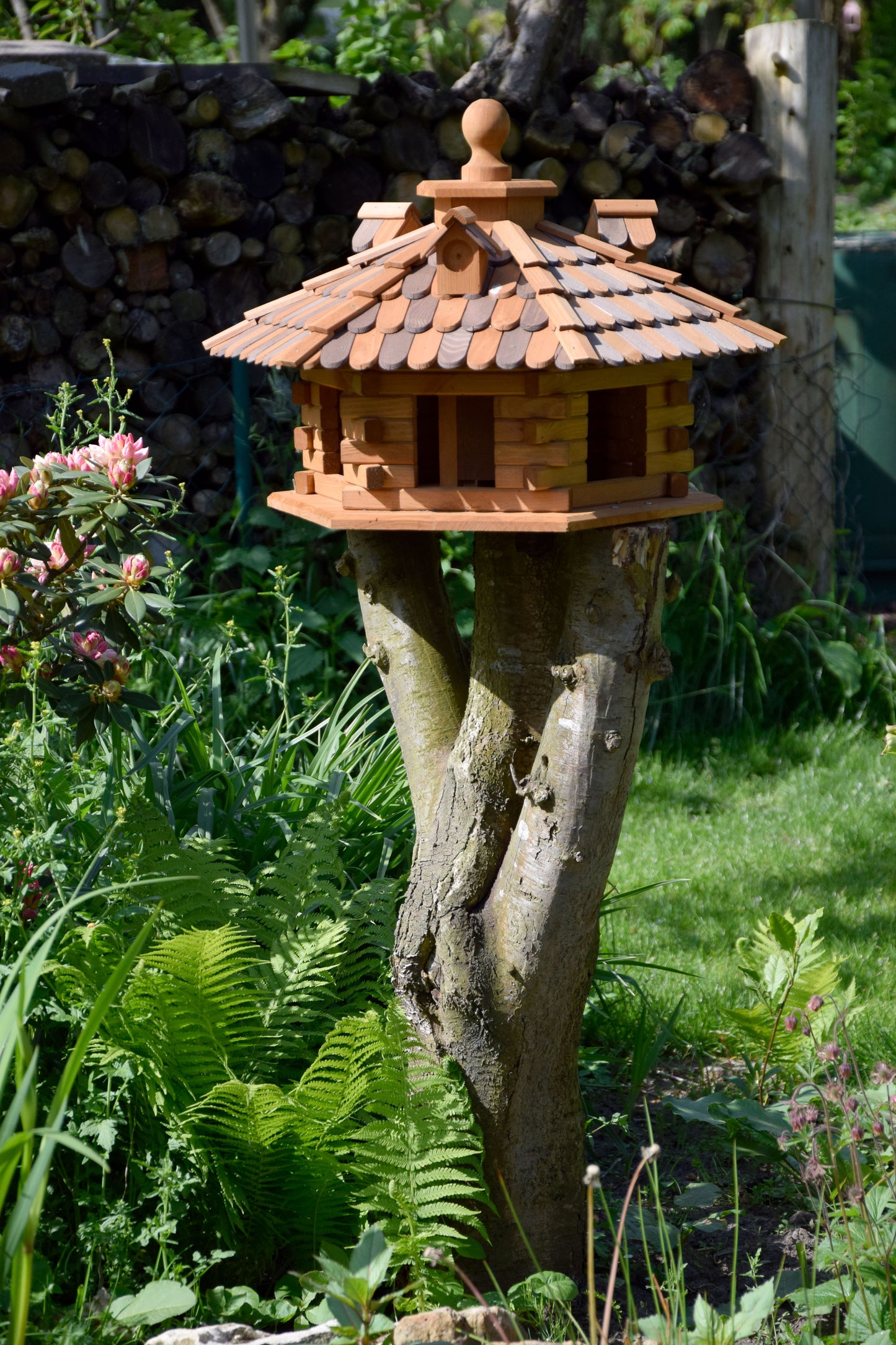 Großes Vogelhaus mit sechseckigem Design und Holzschindeldach, bietet mehreren Wildvögeln gleichzeitig einen Futterplatz.