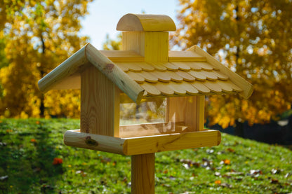 Klassisches Vogelhaus mit wetterfestem Holzschindeldach und Acrylglasscheiben, montiert auf einem Ständer im Garten.