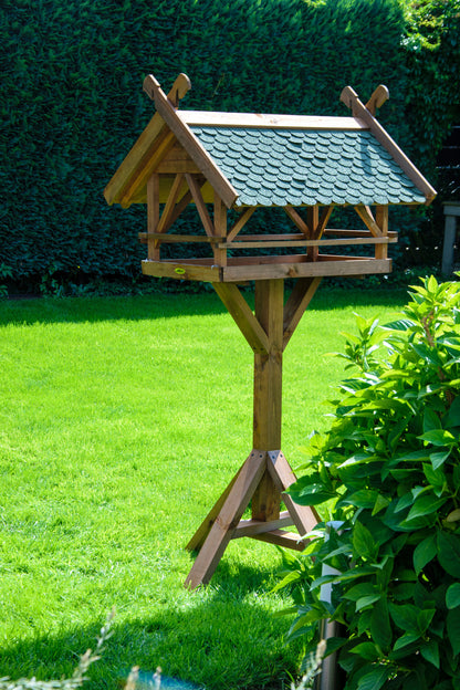 Detailansicht des großen Vogelfutterhauses mit grünem Bitumendach und rustikalem Design.

